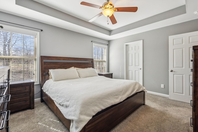 bedroom featuring a tray ceiling, carpet, multiple windows, and baseboards