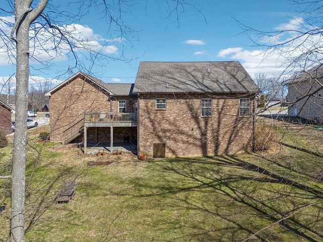 rear view of property featuring a wooden deck, stairway, roof with shingles, a yard, and brick siding