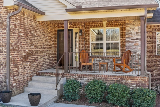 entrance to property with a shingled roof, a porch, and brick siding