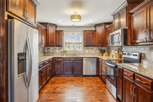 kitchen featuring tasteful backsplash, dark wood-style floors, appliances with stainless steel finishes, light stone countertops, and a sink