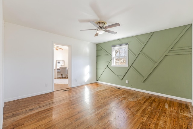 spare room featuring wood finished floors, a ceiling fan, and baseboards