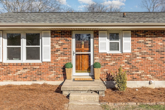 view of exterior entry featuring roof with shingles and brick siding