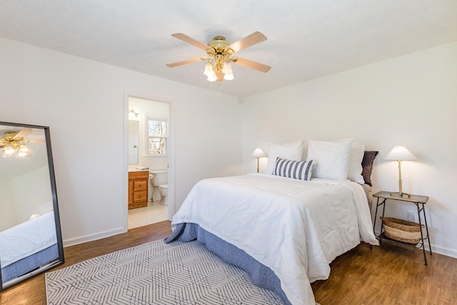 bedroom featuring a ceiling fan, ensuite bath, baseboards, and wood finished floors