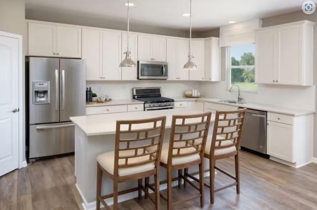 kitchen with wood finished floors, a sink, stainless steel appliances, white cabinetry, and a center island