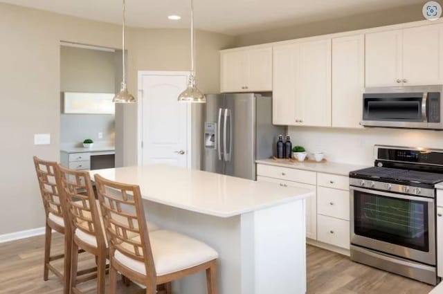 kitchen featuring light wood-style flooring, light countertops, appliances with stainless steel finishes, white cabinetry, and a kitchen bar