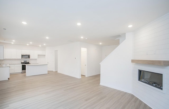 unfurnished living room with recessed lighting, baseboards, a large fireplace, and light wood-style floors