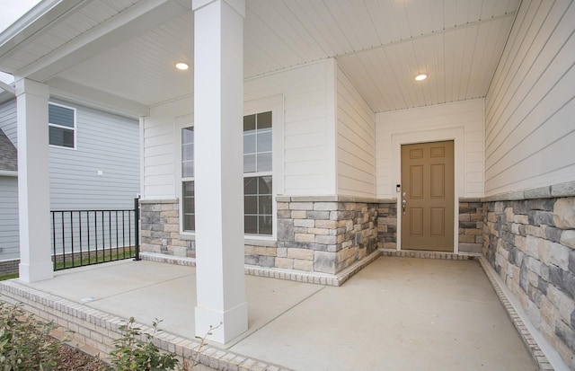 view of exterior entry featuring stone siding and covered porch