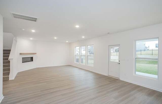 unfurnished living room with visible vents, a large fireplace, stairway, recessed lighting, and light wood-style flooring