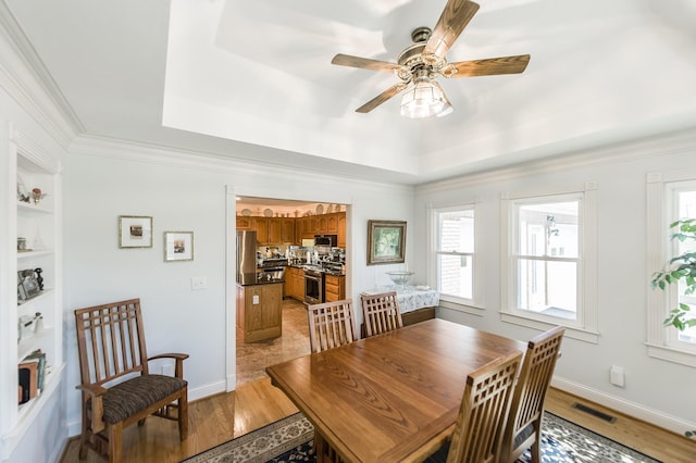 dining area with ornamental molding, light wood-type flooring, a raised ceiling, and visible vents