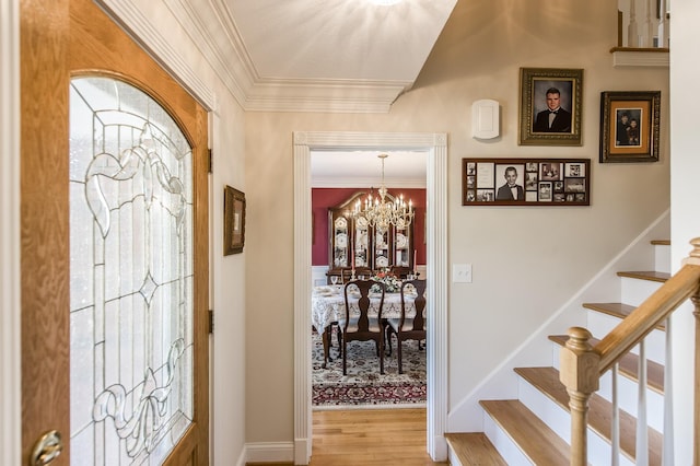 foyer entrance with baseboards, ornamental molding, wood finished floors, an inviting chandelier, and stairs