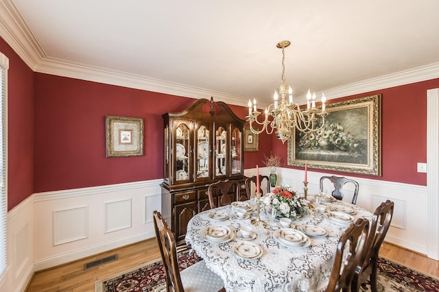 dining space featuring a wainscoted wall, wood finished floors, visible vents, and a chandelier