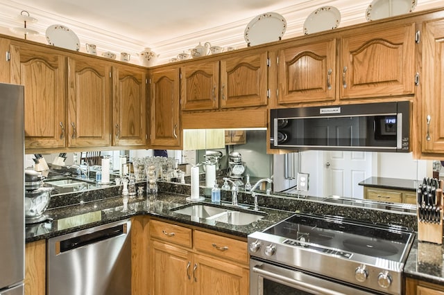 kitchen featuring stainless steel appliances, dark stone counters, brown cabinetry, and a sink