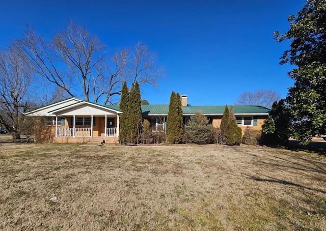 ranch-style house featuring covered porch, metal roof, a chimney, and a front lawn