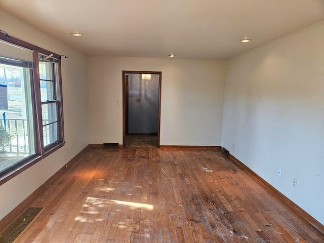 empty room featuring wood-type flooring, visible vents, baseboards, and recessed lighting