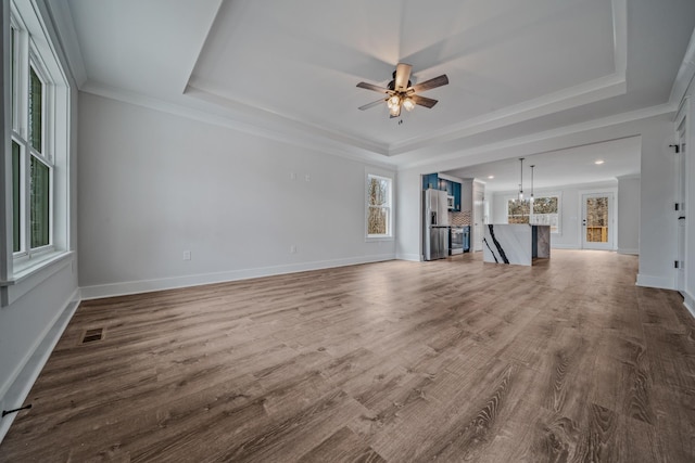 unfurnished living room with a tray ceiling, crown molding, and ceiling fan with notable chandelier