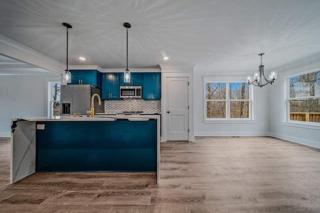 kitchen featuring wood finished floors, appliances with stainless steel finishes, blue cabinetry, decorative backsplash, and a center island with sink