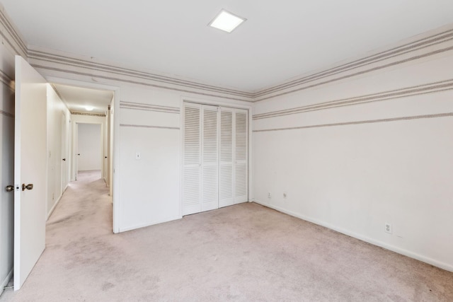 unfurnished bedroom featuring light carpet, ornamental molding, a closet, and baseboards