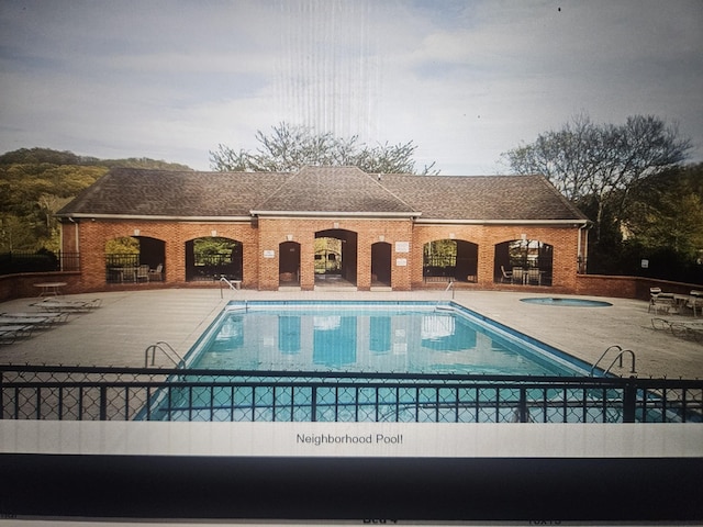 community pool with a patio area, fence, and a hot tub