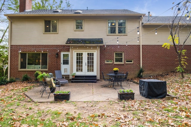 rear view of house featuring entry steps, a patio, brick siding, french doors, and a chimney