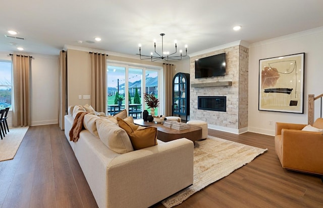 living area featuring a notable chandelier, ornamental molding, wood finished floors, and a stone fireplace