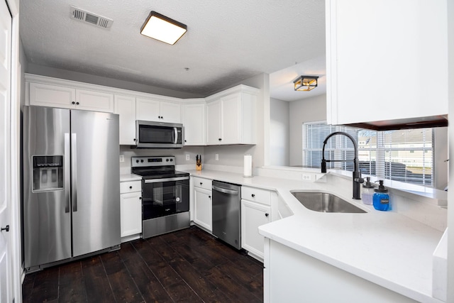 kitchen featuring visible vents, white cabinets, dark wood-style floors, stainless steel appliances, and a sink