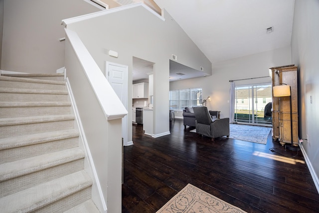 staircase with high vaulted ceiling, visible vents, baseboards, and hardwood / wood-style flooring