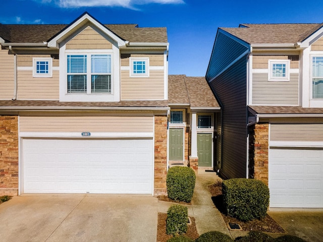 multi unit property featuring a garage, stone siding, driveway, and a shingled roof