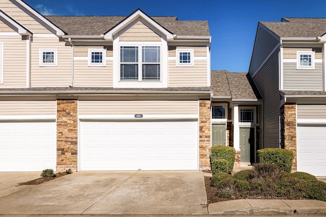 view of property with stone siding, roof with shingles, and concrete driveway