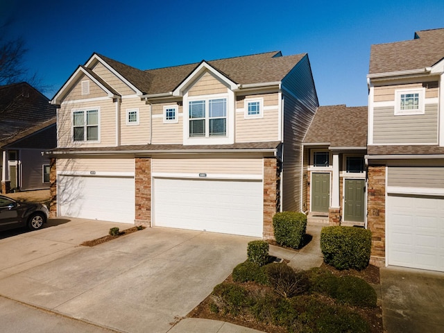 multi unit property with a shingled roof, stone siding, driveway, and an attached garage