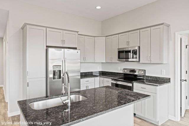 kitchen with light wood finished floors, dark stone countertops, stainless steel appliances, and a sink