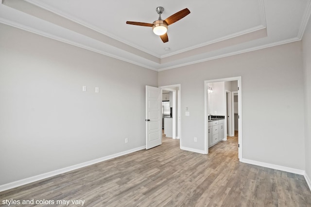 unfurnished bedroom with baseboards, a raised ceiling, ensuite bath, crown molding, and light wood-type flooring