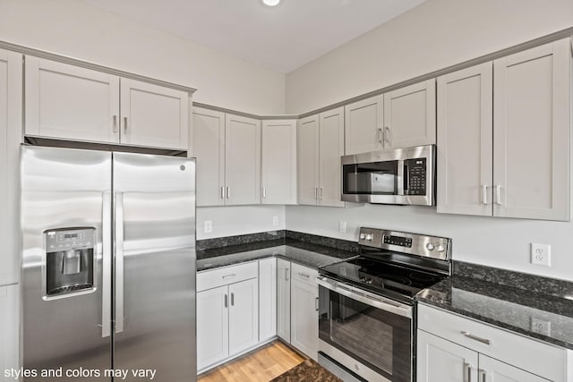 kitchen with light wood-style floors, appliances with stainless steel finishes, dark stone countertops, and recessed lighting