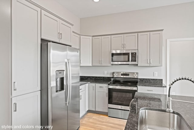 kitchen with dark stone counters, appliances with stainless steel finishes, a sink, and light wood-style flooring