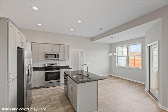 kitchen with light wood finished floors, stainless steel appliances, recessed lighting, a sink, and an island with sink