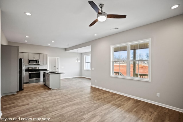 kitchen featuring light wood finished floors, dark countertops, appliances with stainless steel finishes, open floor plan, and baseboards