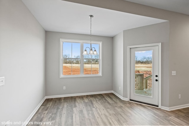 unfurnished dining area featuring a healthy amount of sunlight, baseboards, a chandelier, and wood finished floors