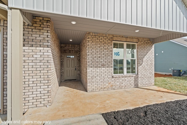 entrance to property featuring central air condition unit, board and batten siding, and brick siding