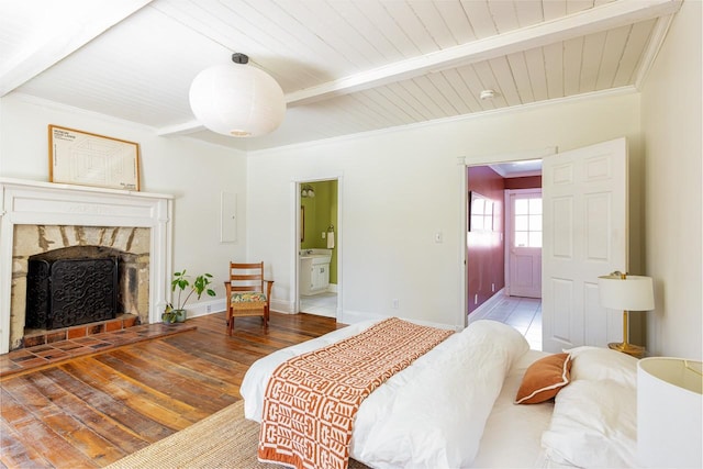 bedroom featuring a stone fireplace, wood finished floors, baseboards, ornamental molding, and beam ceiling