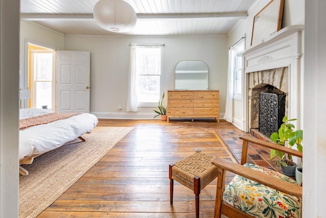 bedroom featuring wood-type flooring, a fireplace, baseboards, and beamed ceiling