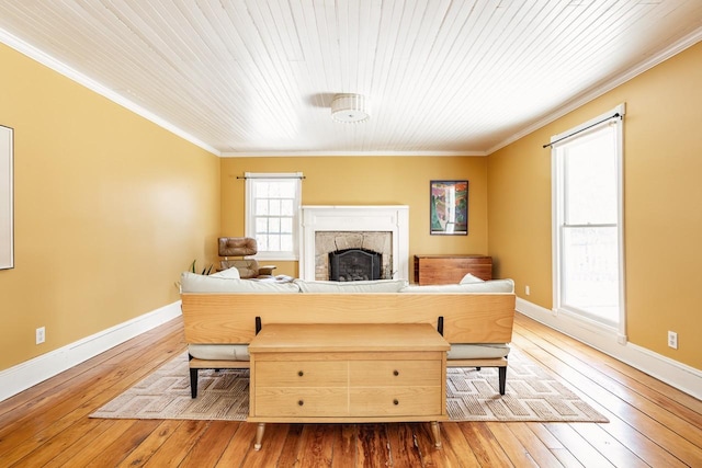 living area with wood-type flooring, a fireplace, ornamental molding, and baseboards