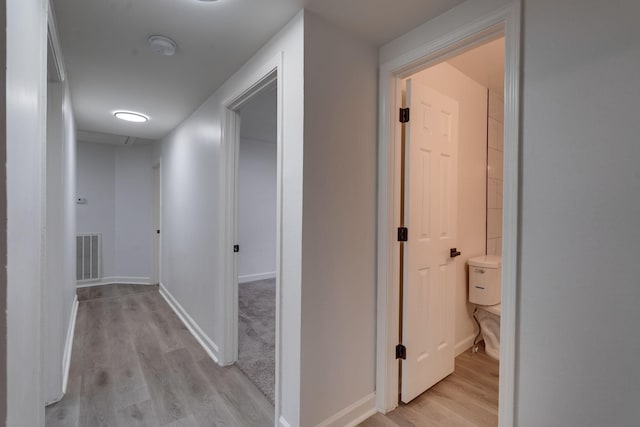 corridor with light wood finished floors, visible vents, and baseboards