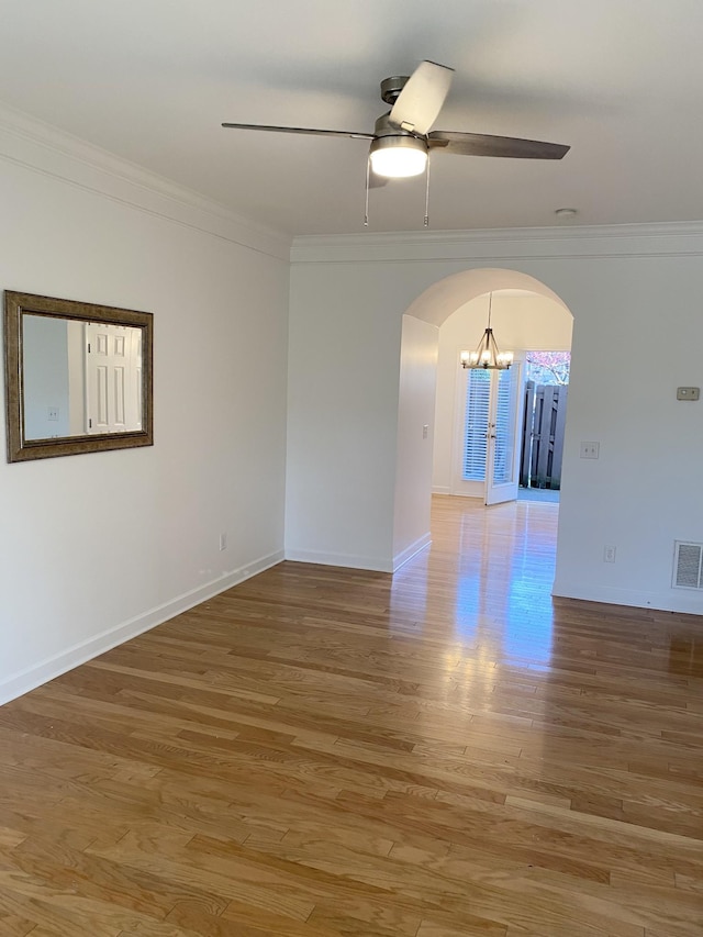 spare room with arched walkways, light wood-style floors, ornamental molding, ceiling fan, and baseboards