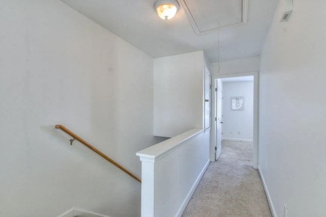 corridor featuring light carpet, an upstairs landing, attic access, and baseboards