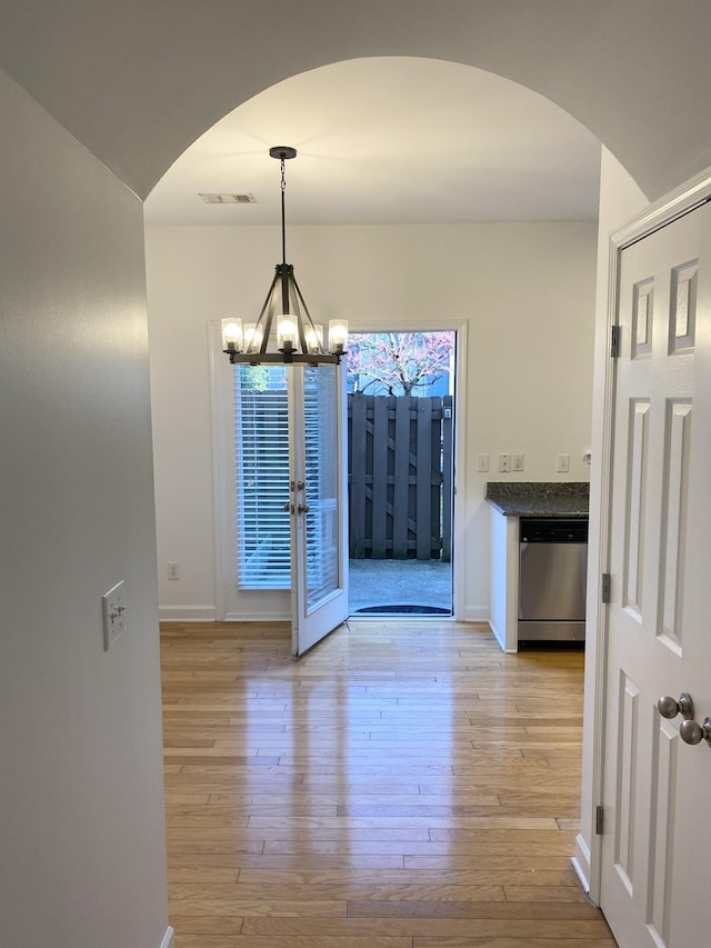 unfurnished dining area featuring baseboards, visible vents, arched walkways, light wood-style flooring, and a notable chandelier