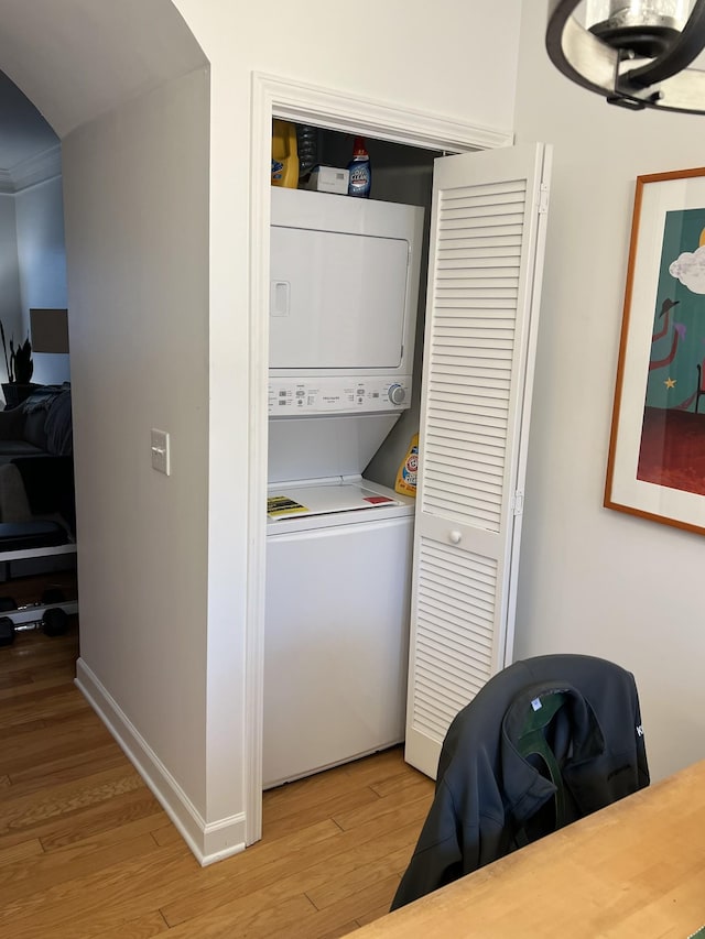 clothes washing area featuring light wood-type flooring, stacked washer / drying machine, laundry area, and baseboards