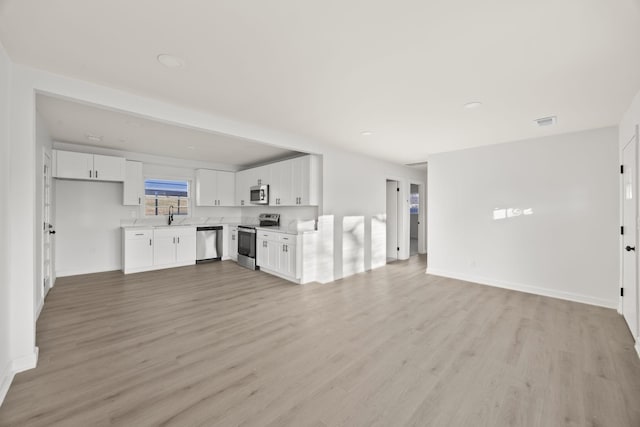 unfurnished living room featuring light wood-style floors, baseboards, visible vents, and a sink