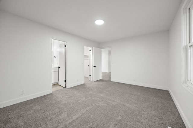 unfurnished bedroom with carpet floors, connected bathroom, a spacious closet, and baseboards