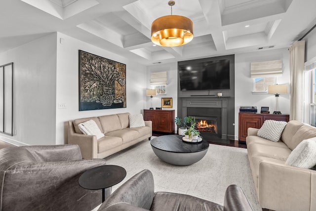 living area with coffered ceiling, wood finished floors, visible vents, beam ceiling, and a glass covered fireplace