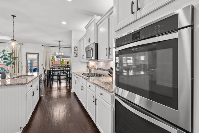 kitchen featuring light stone counters, a sink, appliances with stainless steel finishes, decorative backsplash, and dark wood-style floors