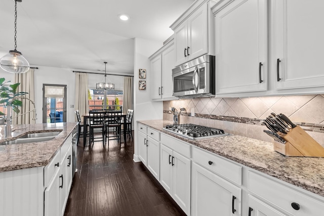 kitchen with light stone counters, a sink, appliances with stainless steel finishes, dark wood-style floors, and tasteful backsplash